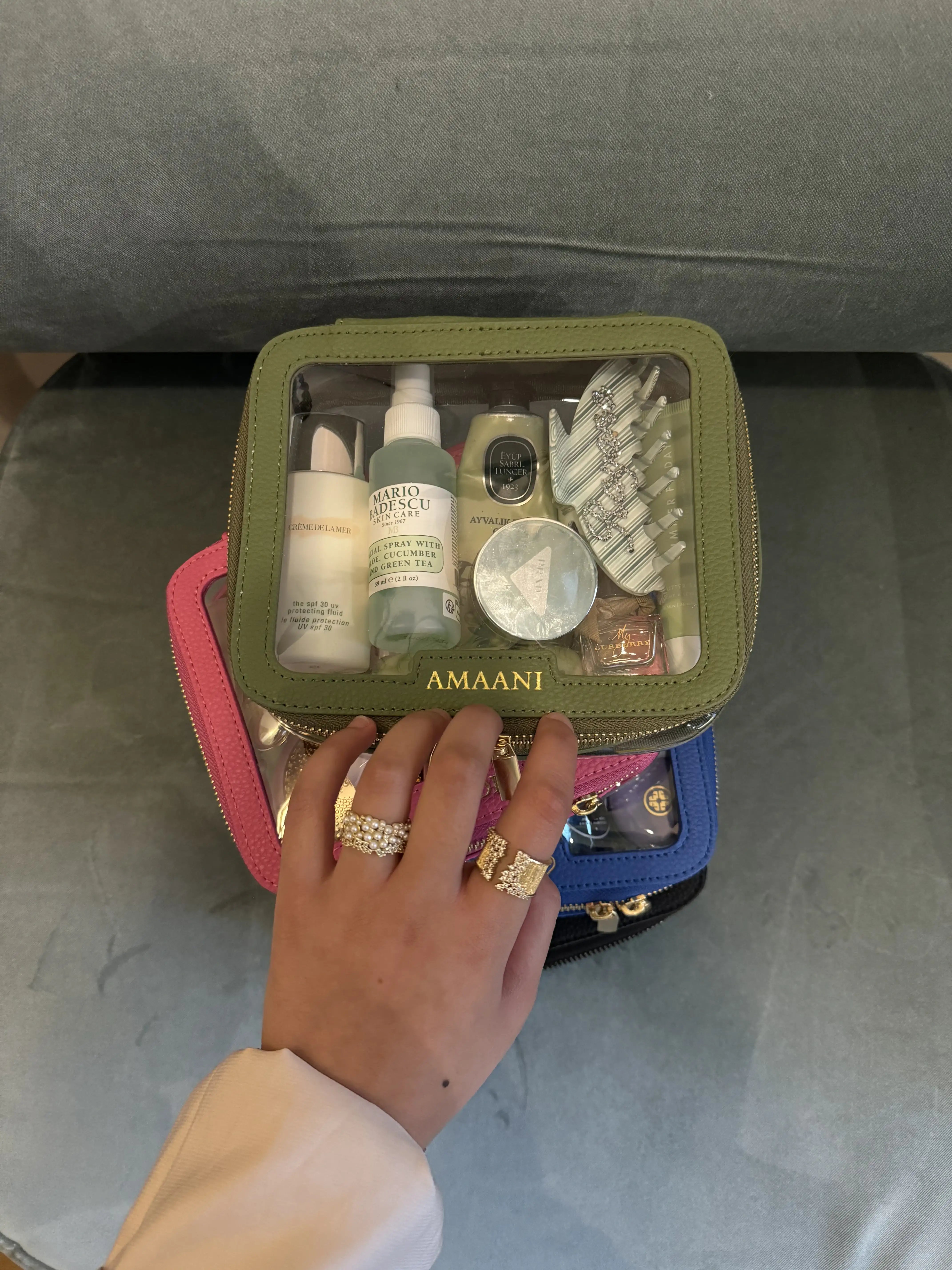 Hand holding a personalised green clear makeup bag filled with skincare and beauty items.